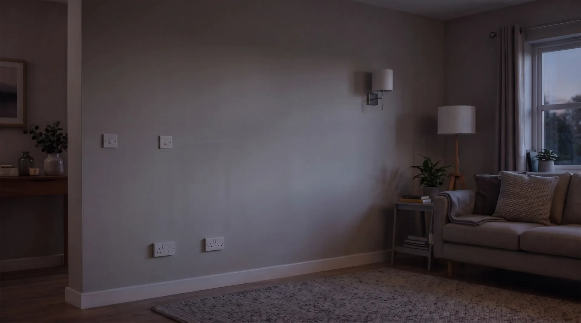 A calm living room at dusk with a plain wall, sockets and a wall light