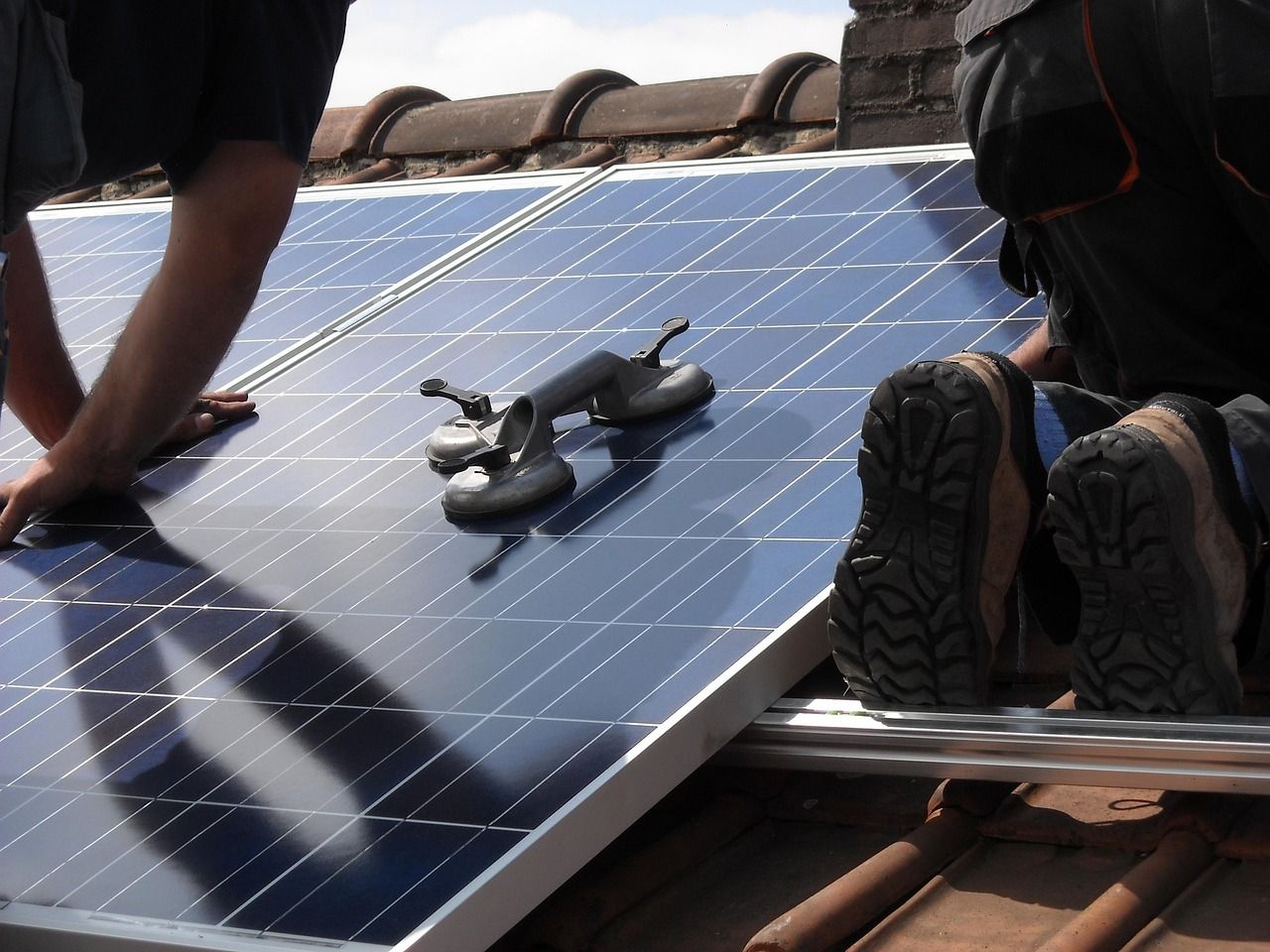Installers fitting a solar panel onto a tiled roof